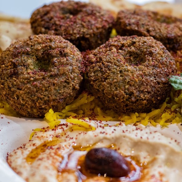Four falafel balls with yellow rice, hummus, olive, and spices in a white bowl.
