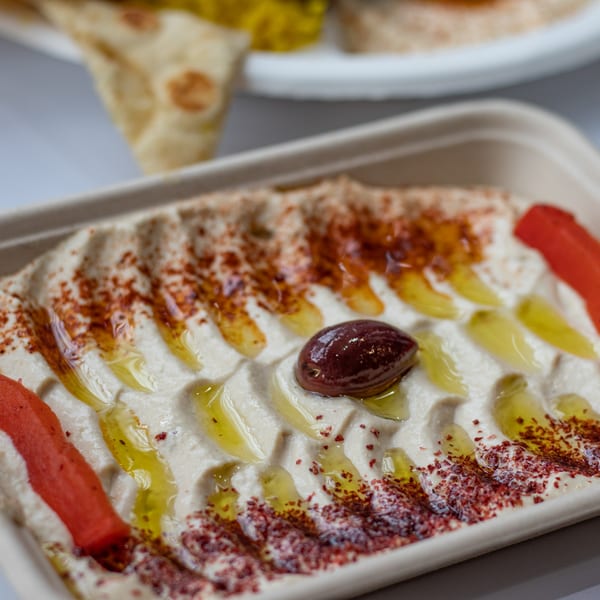 Creamy hummus drizzled with olive oil, sprinkled with paprika, and garnished with an olive and red pepper.