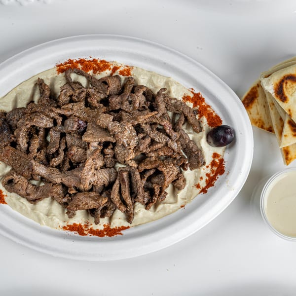 Niro's Gyros beef shawarma plate with hummus, paprika, an olive, pita bread, and tahini sauce.