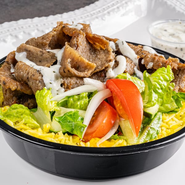 Niro's Gyros bowl with sliced meat, lettuce, tomatoes, onions, yellow rice, and white sauce.