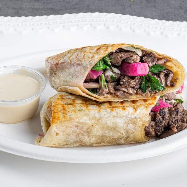 Two halves of a gyro wrap filled with meat, pickled turnips, and parsley, with a side of sauce.