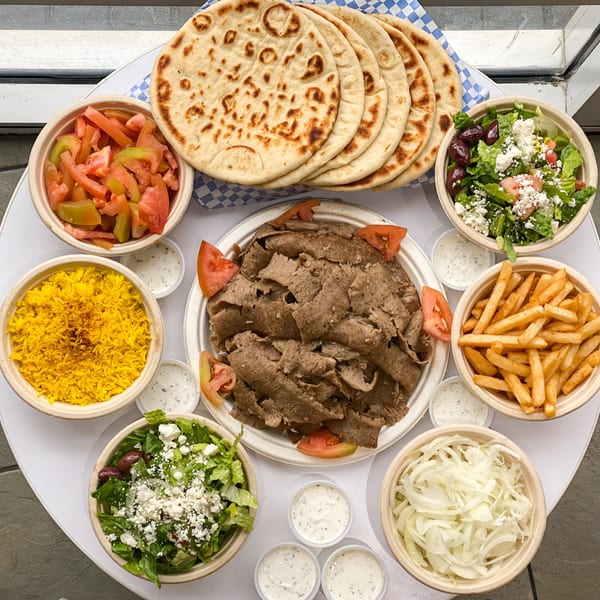 A Greek feast with gyro meat, pita bread, rice, fries, salads, tomatoes, onions, and tzatziki.