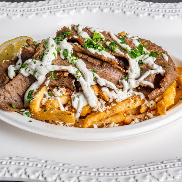 Niro's Gyros plate with sliced meat, french fries, feta, tzatziki, parsley, and a lemon wedge.