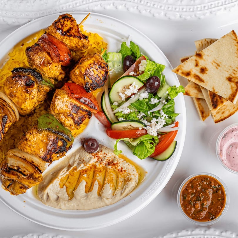 Niro's Gyros chicken souvlaki plate with rice, Greek salad, hummus, pita bread, and sauces.