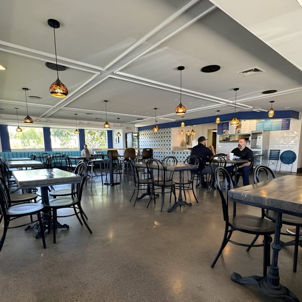 Interior of Niro's Gyros, a Greek restaurant, with tables, chairs, and two men seated.