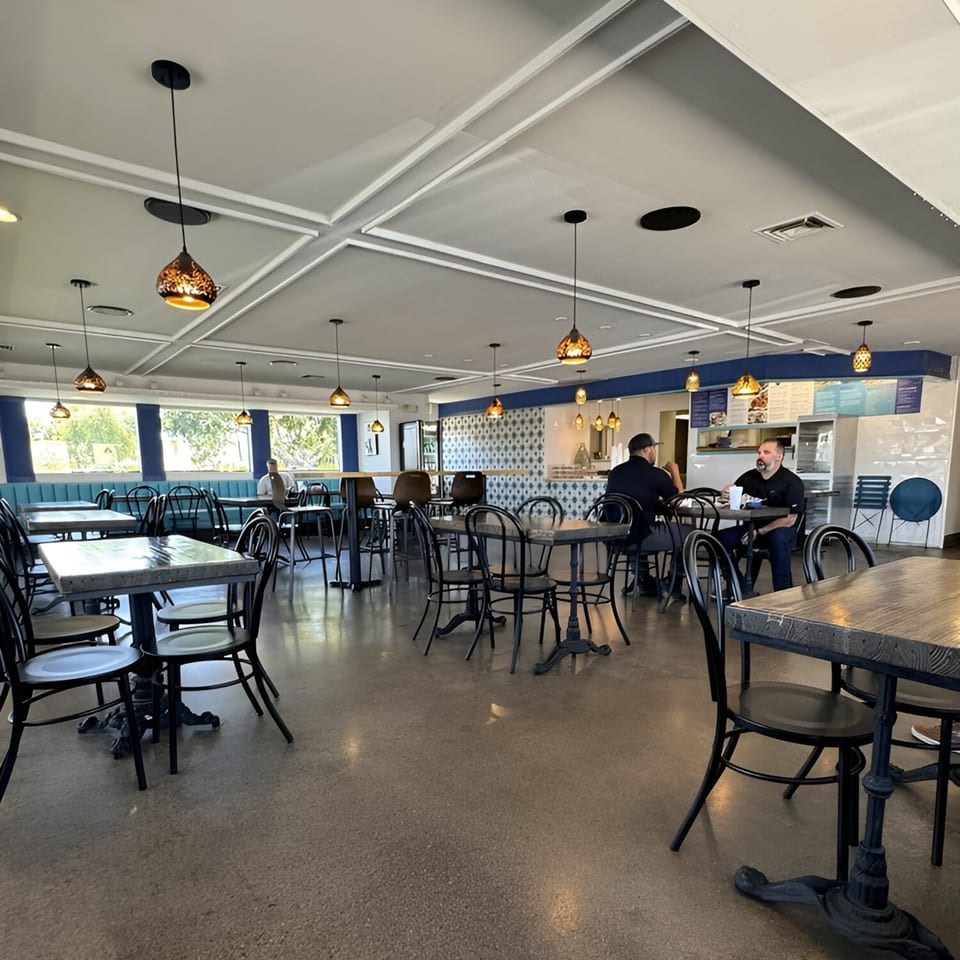 Interior of Niro's Gyros, a Greek restaurant, with tables, chairs, and two men seated.